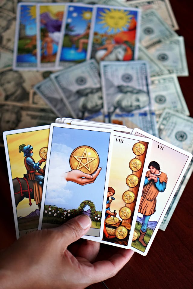 Tarot and Currency: Symbolizing Financial Manifestation and Abundance Hand holding tarot cards with pentacles imagery, laid over US dollar bills and additional tarot cards in the background, symbolizing affirmations for money and financial manifestation.