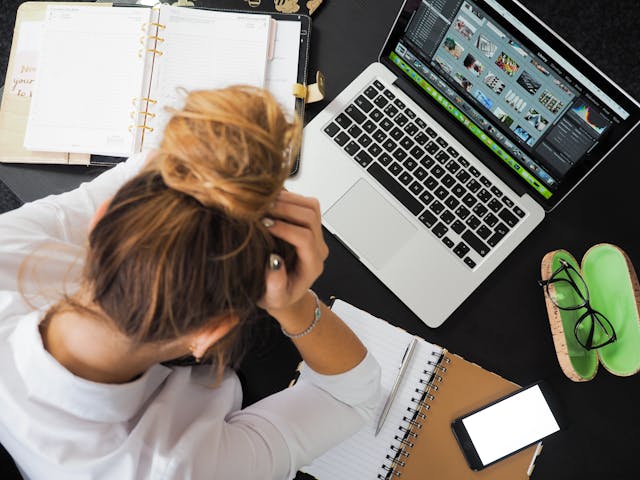 Stressed woman at desk surrounded by work tools, symbolizing the mental clutter that blocks clarity on how to control my reality