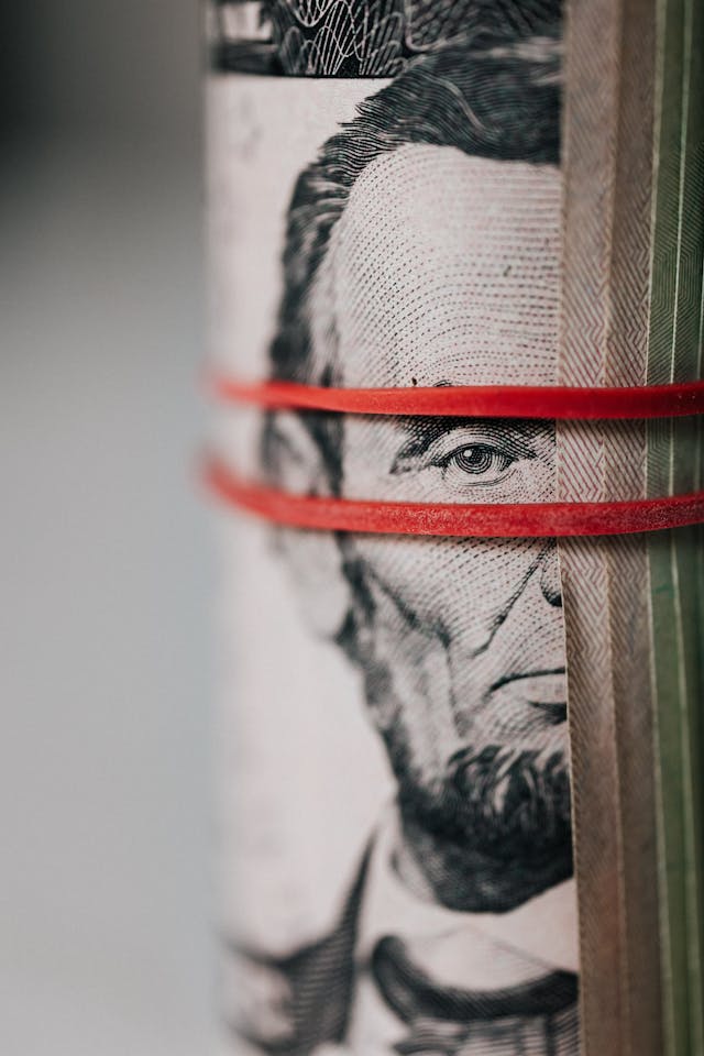 Rolled U.S. Currency Secured with Red Rubber Bands Close-up of a rolled U.S. five-dollar bill wrapped with red rubber bands, showing Abraham Lincoln’s face.