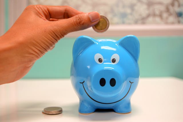 Saving for Abundance: The Joy of Financial Growth A hand placing a coin into a smiling blue piggy bank, symbolizing financial freedom affirmations and joyful money habits