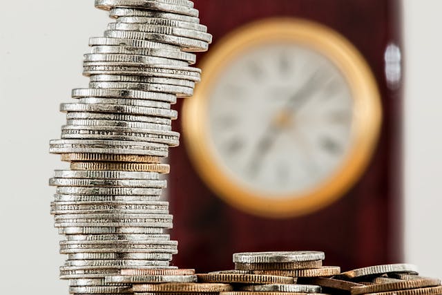 Wake Up from the Matrix: Stop Trading Time for Money Leaning stack of silver coins in front of a blurred clock, symbolizing trading time for money