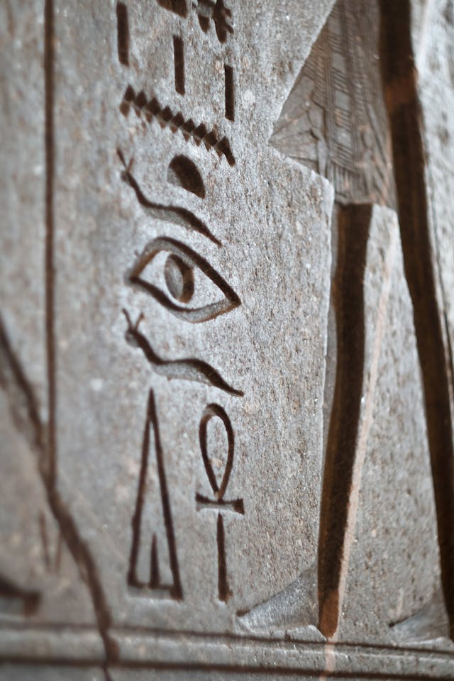 Ancient Eye of Horus Symbol Linked to Pineal Gland Frequencies in Egyptian Hieroglyphs Close-up of Egyptian hieroglyphs engraved in stone, featuring ancient symbols like the Eye of Horus and Ankh, often associated with pineal gland frequencies.