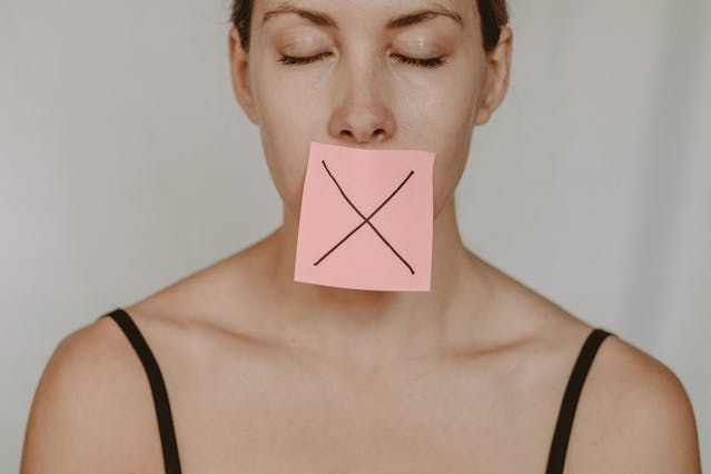 Silenced Truth: The Price of Keeping the Peace woman with a pink sticky note X over her mouth showing signs you sold your soul by suppressing your voice
