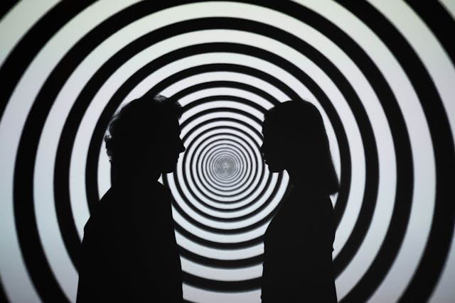 Two silhouettes facing each other against a hypnotic spiral, illustrating how to rewire your mind by reprogramming early subconscious patterns