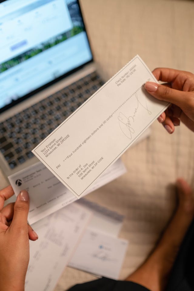 Hands holding a paycheck in front of a laptop, symbolizing financial flow and abundance through manifestation practices
