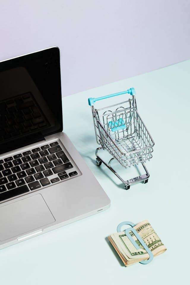 Laptop with a miniature shopping cart and stack of U.S. dollars, illustrating how to stop being broke by creating online income streams