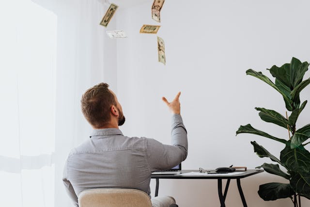 A guy sitting at his desk throwing money in the air symbolising EFT Tapping for Manifesting Money