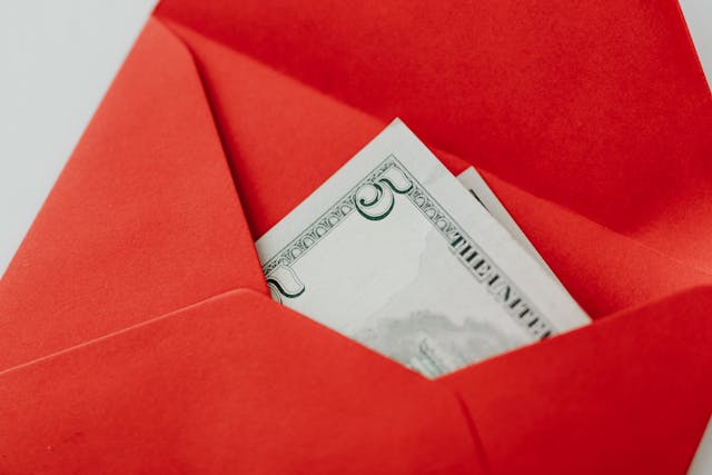Red envelope with U.S. cash peeking out, symbolizing “how did Bob Proctor make his money” and the idea that money is a reward for service and value