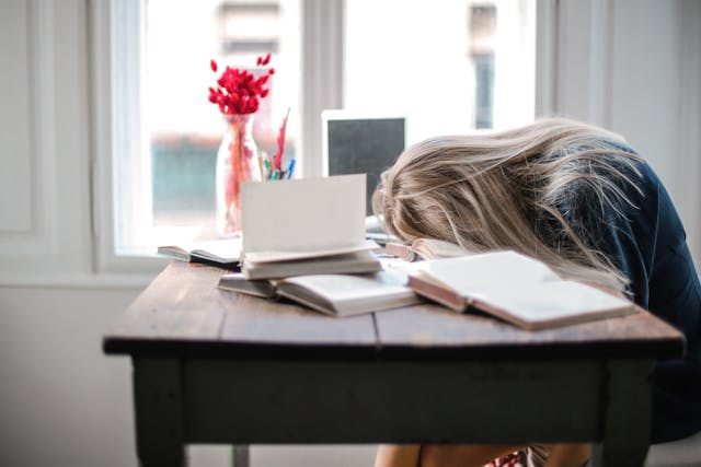 Tired woman with head on a desk surrounded by open notebooks, illustrating overwhelm before applying the jack canfield rule of 5.