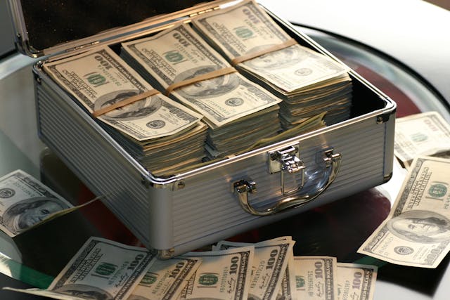 Open silver briefcase filled with stacks of hundred-dollar bills, representing wealth and millionaire mindset secrets.
