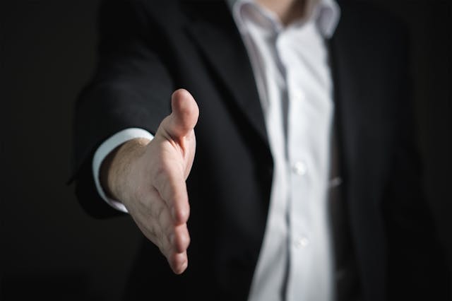 Businessman in a suit extending a handshake, symbolizing how to stop being broke by creating opportunities and building strong financial relationships
