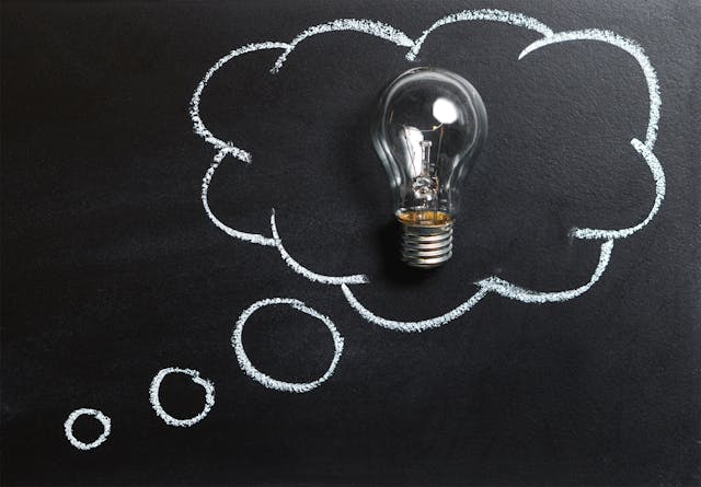 Clear lightbulb placed inside a chalk-drawn thought bubble on a blackboard, symbolizing ideas and creative thinking