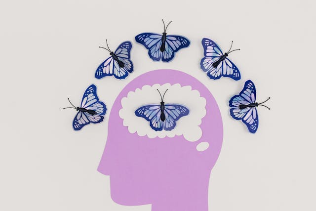 Change Reality With Your Mind: Thought Transformation Purple paper silhouette of a head with blue butterflies circling the brain, symbolizing changing reality with your mind.