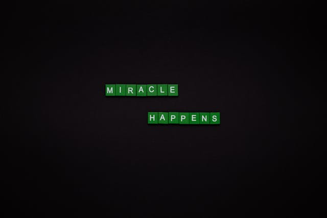 How to Manifest Miracles in Your Life Green letter tiles spelling “Miracle Happens” on a dark background.