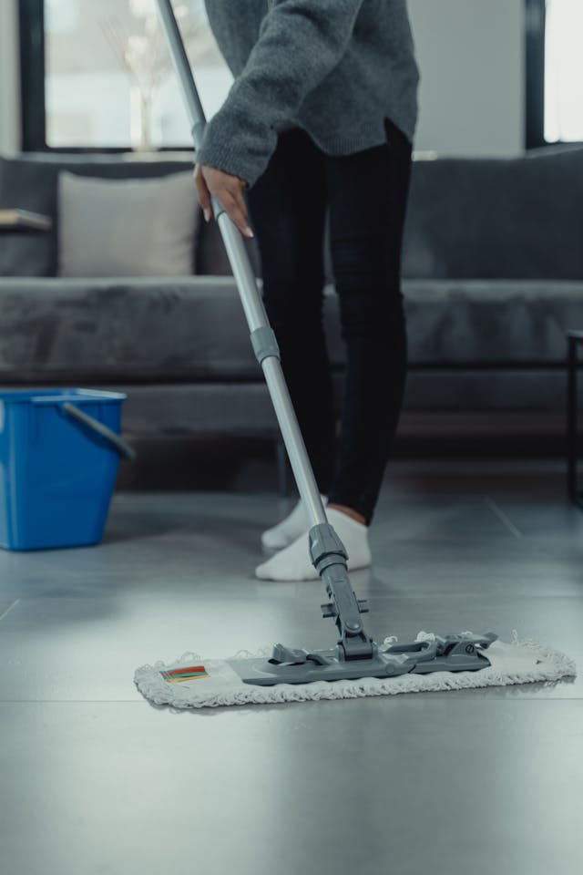 Person mopping a floor with a blue bucket nearby, illustrating “how did Bob Proctor make his money” by starting as a janitor before transforming his mindset and income