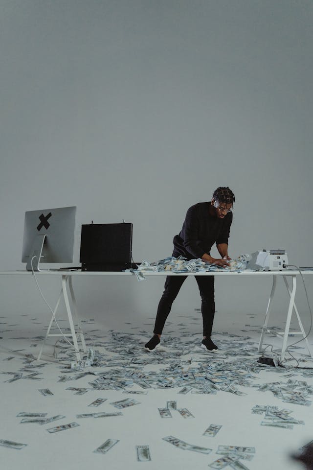 Man in a minimalist studio surrounded by scattered dollar bills at a desk with a laptop and cash counter, symbolizing affirmations for financial freedom and abundant cash flow