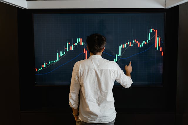 Man studying a stock market chart on a large screen, representing financial growth and millionaire mindset secrets to raise income.