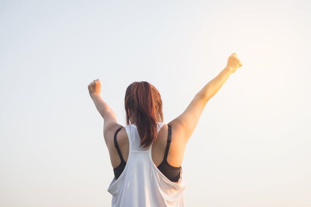 Morning Victory Energy Person outdoors raising arms in triumph at sunrise, celebrating a fresh start.