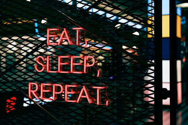 Neon sign reading “EAT, SLEEP, REPEAT,” representing how to rewire your mind by replacing automatic loops with empowering routines