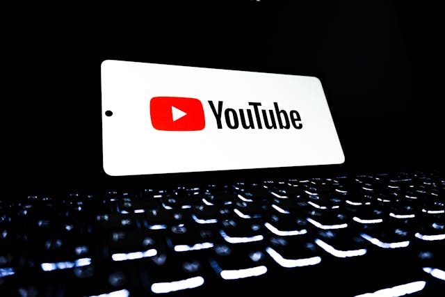 YouTube logo on a smartphone screen above a glowing computer keyboard in a dark setting