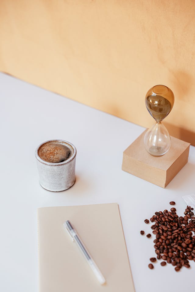 Minimalist desk with notebook, pen, hourglass, and coffee—tools for how to manifest while sleeping and review in the morning