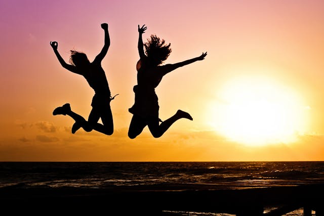 Joyful Energy: How to Raise Your Vibration to Manifest Two people jumping on the beach at sunset showing how to raise your vibration to manifest joy and abundance