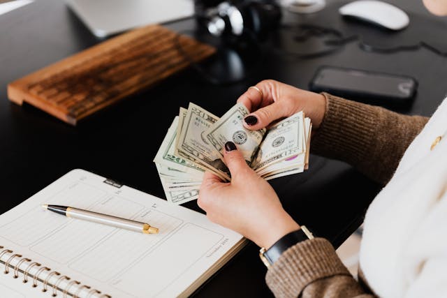 Smart Money Habits: How Can You Increase Your Income Person counting stacks of dollar bills at a desk, representing how can you increase your income with better money management