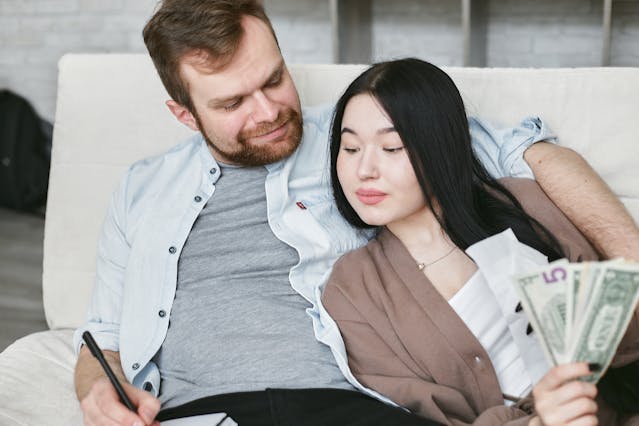 Couple sitting together with money and a notebook, symbolizing how thoughts create reality and financial abundance