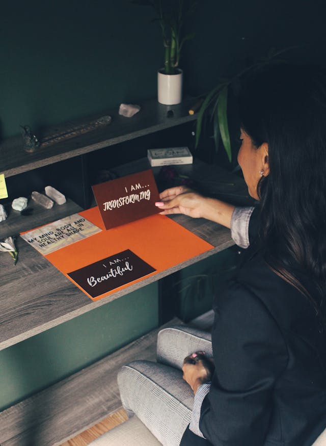 Woman arranging handwritten “I am” notes on a desk—how to make affirmation cards with simple supplies