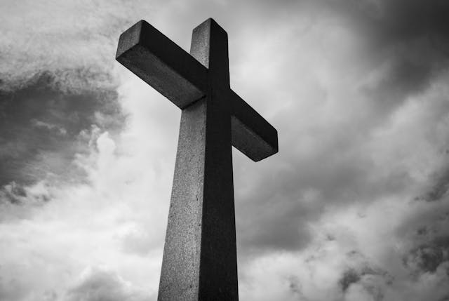 Stone Cross Under Storm Clouds Black-and-white stone cross against storm clouds—a quiet call to ask god to guide you.