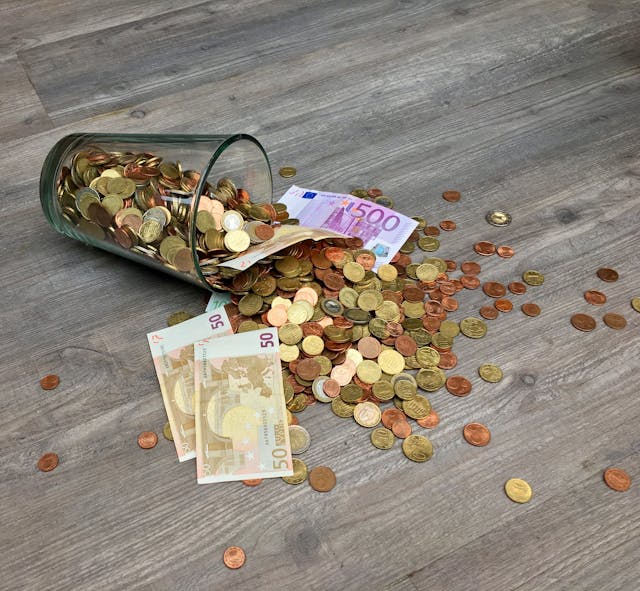 Overflowing Abundance: Manifestation Quotes for Money in Action Glass jar spilling coins and euro banknotes onto the floor, symbolizing manifestation quotes for money