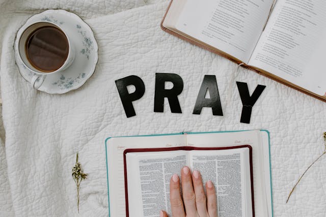 Flat lay of open Bibles, coffee cup, and letters spelling PRAY on a white blanket, highlighting ask believe receive scripture.