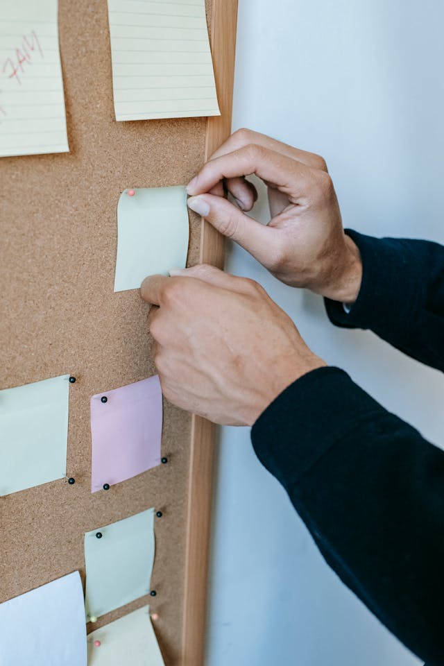 Hands pinning colorful sticky notes on a corkboard, illustrating what is subconscious reprogramming through daily affirmations and habit tracking