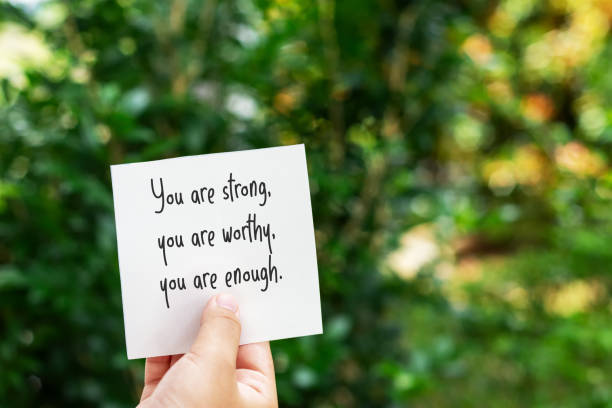 A hand holds a white note that reads “You are strong, you are worthy, you are enough,” symbolizing encouragement and the power of daily affirmations for self worth.