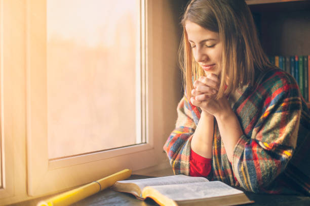 What Does Affirmation Mean in the Bible — Speak Life at Dawn Woman praying with clasped hands over an open Bible by a sunlit window — what does affirmation mean in the Bible.