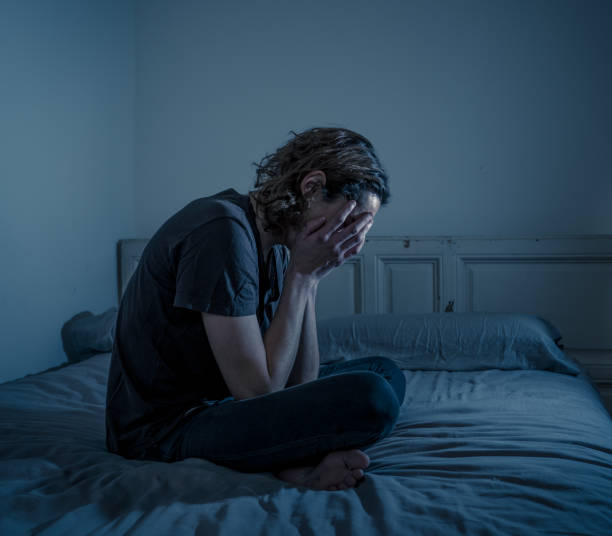 A person sits on a bed in a dimly lit room with their face in their hands, representing emotional struggle before practicing daily affirmations for self worth.