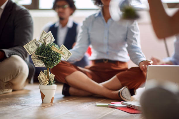 Group of people meditating on the floor with a small money tree decorated with dollar bills, symbolizing powerful money affirmations that work with calm focus.