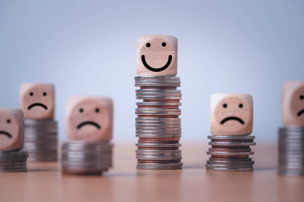 Happy face block on the tallest stack of coins among smaller, sad stacks — financial miracles mindset.