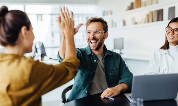 You’re Hired — Prayer to Get a Job in Action Coworkers high-five at a desk with a laptop, celebrating success after a prayer to get a job.