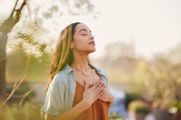 Peaceful Heart — One Word Manifestation in Practice A woman outdoors with her eyes closed and hands on her heart, breathing deeply in sunlight, embodying the feeling of gratitude and one word manifestation.