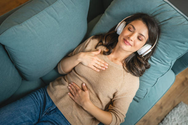 Relaxation and Visualization — Daily Manifestation Routine in Action A woman rests on a couch with headphones, eyes closed, and a hand on her heart, visualizing goals as part of her daily manifestation routine.