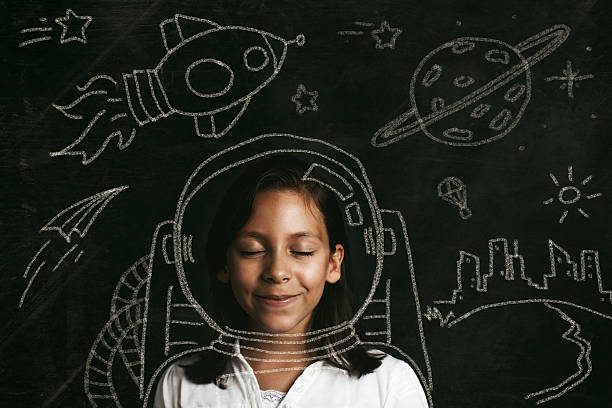 Smiling child with eyes closed in front of chalk-drawn spacesuit, rockets, and planets, illustrating visualization used in hypnosis to get rich.