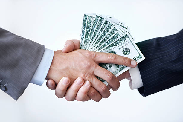 Business handshake with cash between two people, symbolizing deals created through 10 money affirmations that really work.