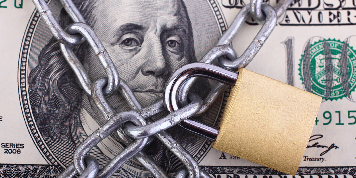 Close-up of a U.S. hundred dollar bill wrapped in heavy metal chains and secured with a brass padlock, symbolizing restricted wealth and financial limitation.