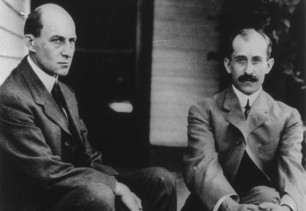 Historic black and white photograph of Wilbur and Orville Wright seated side by side, dressed in early 20th-century suits.