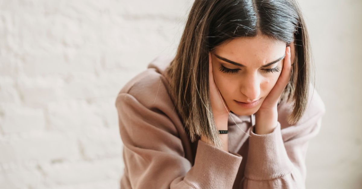Woman sitting with her head in her hands looking stressed and overwhelmed while thinking deeply.