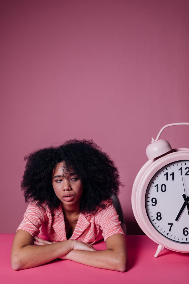 Stop Waiting: Words to Avoid When Manifesting Woman sitting beside a large clock looking tired and waiting, illustrating words to avoid when manifesting like waiting and delay